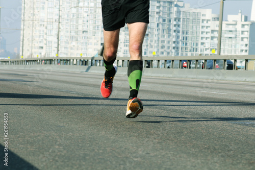 Young man running on city bridge road. Marathon running in the morning light . Running on city road. Athlete runner feet running. Blured city background