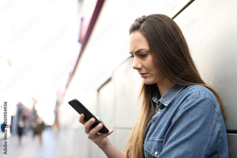 Sad woman checking smart phone content in the street Sad woman checking smart phone content in the street