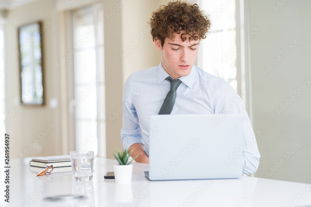 Young business man working with computer laptop at the office with hand on stomach because nausea, painful disease feeling unwell. Ache concept.