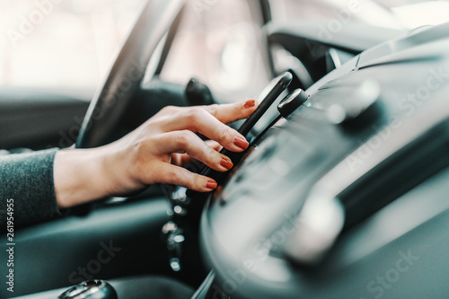 Close up of young Caucasian woman driving car and using smart phone.