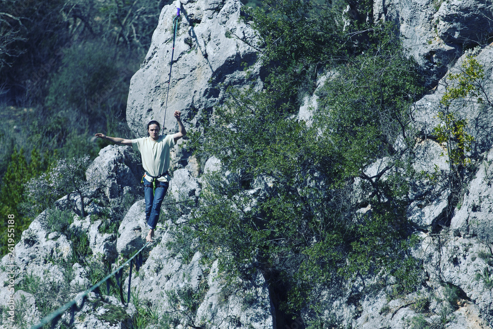 A man is walking along a stretched sling. Highline in the mountains. Man catches balance. Performance of a tightrope walker in nature. Highliner on the background of valley. A man is walking along a stretched sling. Highline in the mountains. Man catches balance. Performance of a tightrope walker in nature. Highliner on the background of valley.