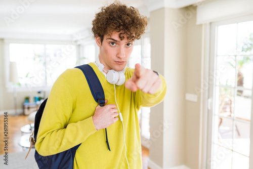 Young student man wearing headphones and backpack pointing with finger to the camera and to you, hand sign, positive and confident gesture from the front © Krakenimages.com
