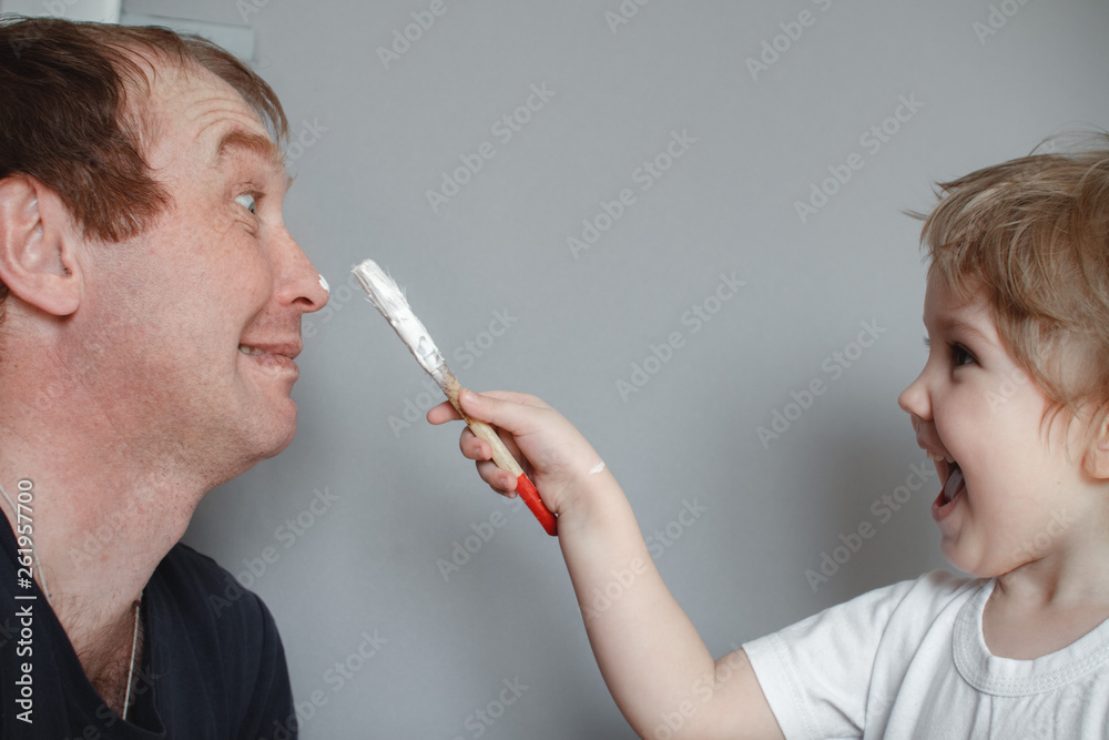 Obraz premium The concept of family. The child draws a brush on the nose of his father. Father and daughter at home having fun