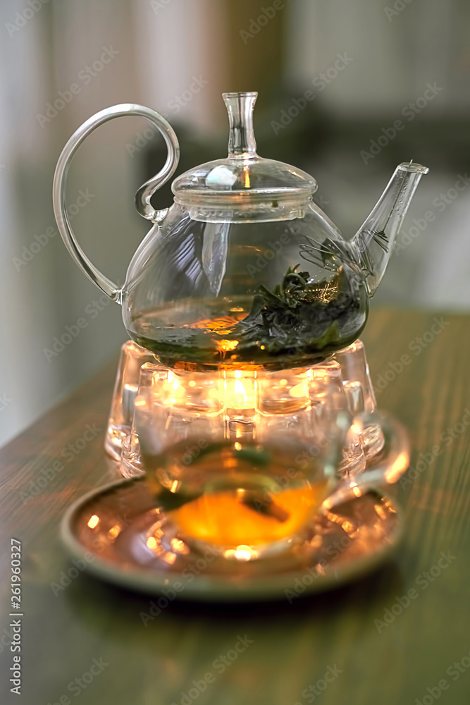 Transparent teapot with green tea on a stand with a candle, close-up Transparent teapot with green tea on a stand with a candle, close-up