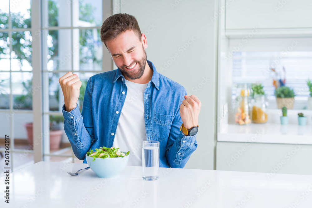 Handsome man eating fresh healthy salad very happy and excited doing winner gesture with arms raised, smiling and screaming for success. Celebration concept. Handsome man eating fresh healthy salad very happy and excited doing winner gesture with arms raised, smiling and screaming for success. Celebration concept.