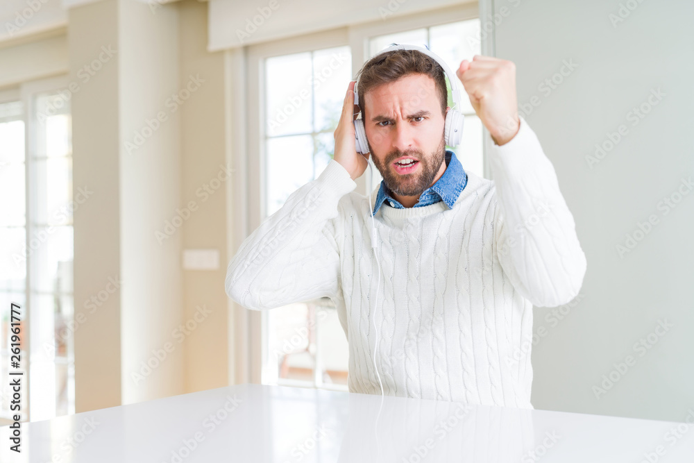 Handsome man wearing headphones and listening to music annoyed and frustrated shouting with anger, crazy and yelling with raised hand, anger concept