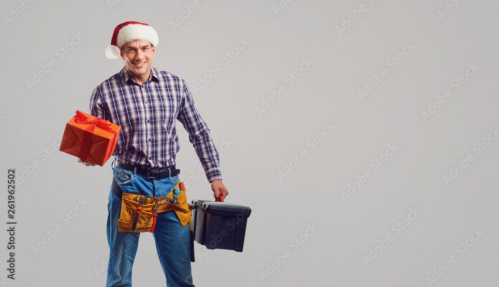 Repairman in Santa hat with a gift on a gray background. Repairman in Santa hat with a gift on a gray background.