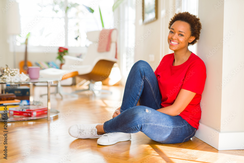 Beautiful young african american woman smiling confident to the camera showing teeth sitting on the floor at home