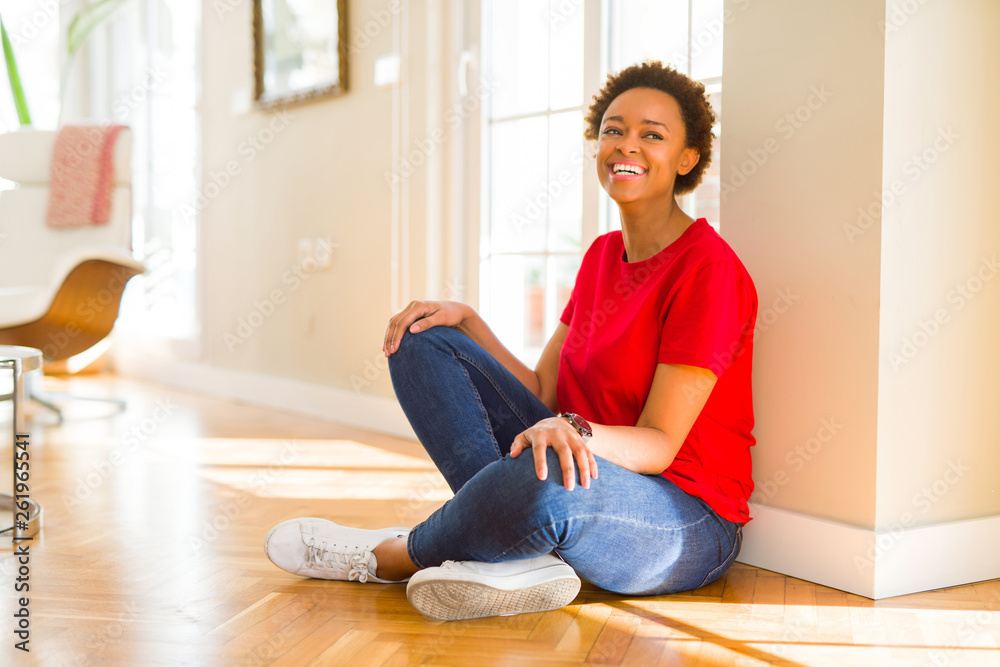 Beautiful young african american woman smiling confident to the camera showing teeth sitting on the floor at home