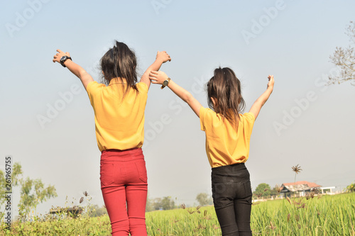 Two child girls in a field and their hands are raised up to the sky