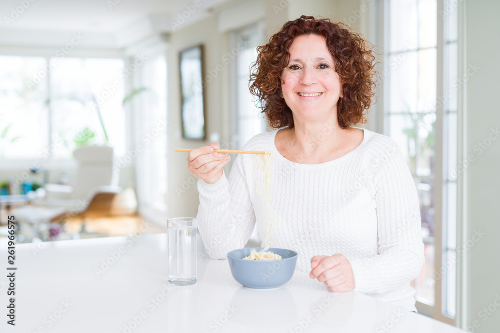 Senior woman eating asian noodles using chopsticks with a happy face standing and smiling with a confident smile showing teeth Senior woman eating asian noodles using chopsticks with a happy face standing and smiling with a confident smile showing teeth