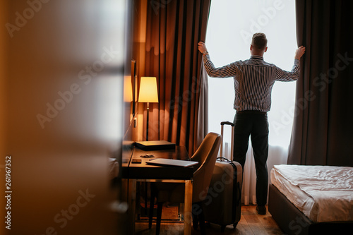 Businessman at a hotel room opening the curtains. Manager standing next to the window, opens the curtains. 