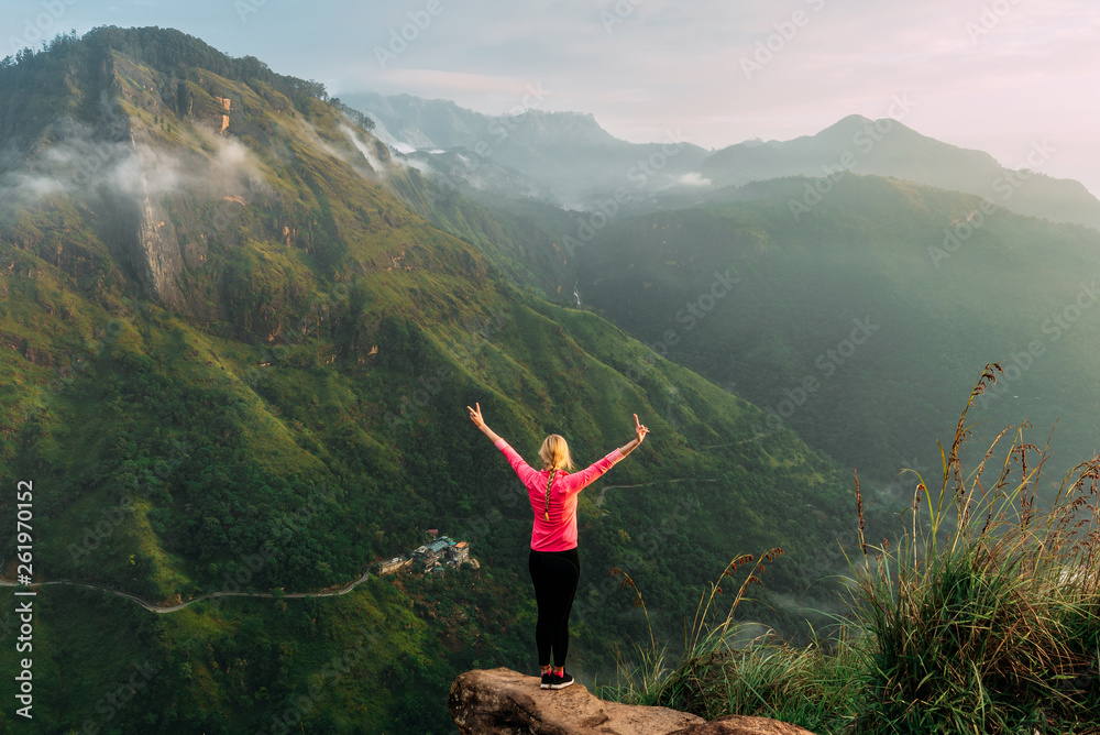 Girl meets sunrise in the mountains. Girl traveling to Sri Lanka. Mountain sports. Athlete happy finish. Mountain tourism. Walking tour. The journey to the mountains. Nordic walking. Rear view