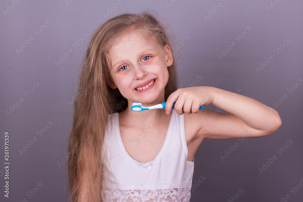 Concept of caring for the teeth. Little smiling girl brushing her teeth over grey Concept of caring for the teeth. Little smiling girl brushing her teeth over grey