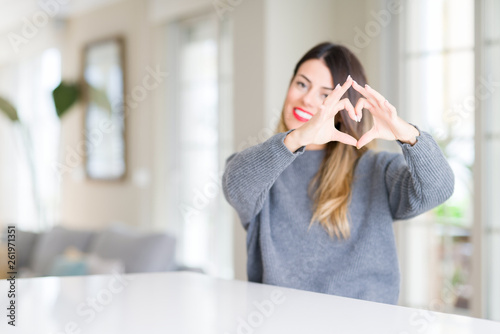 Young beautiful woman wearing winter sweater at home smiling in love showing heart symbol and shape with hands. Romantic concept.