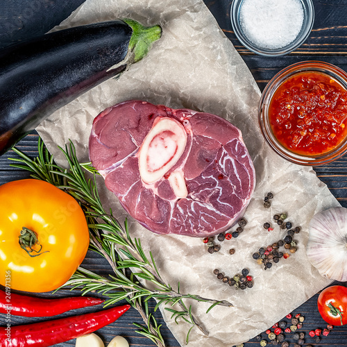 raw pork steak on a dark black background on white craft paper between spices anh herbs, salt, pepper, rosemary, Ready to cook or grill photo