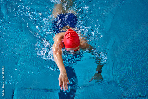 Female athlete swimming fast in crawl style. Splashes of water scatter in different directions.