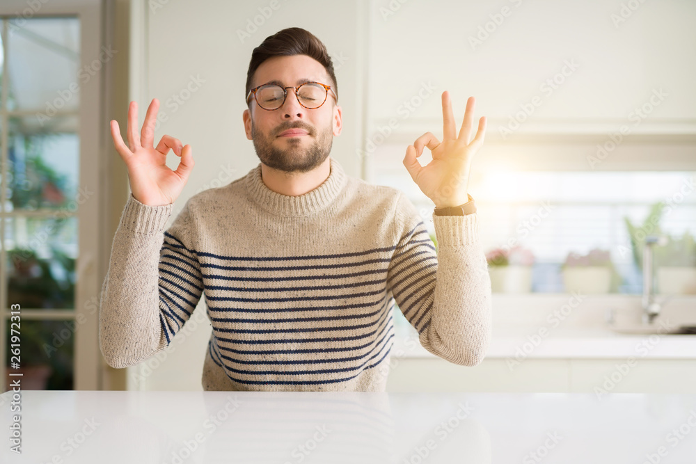 Young handsome man wearing glasses at home relax and smiling with eyes closed doing meditation gesture with fingers. Yoga concept.