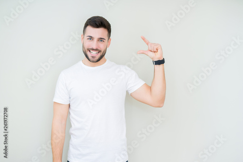 Young handsome man wearing casual white t-shirt over isolated background smiling and confident gesturing with hand doing size sign with fingers while looking and the camera. Measure concept.