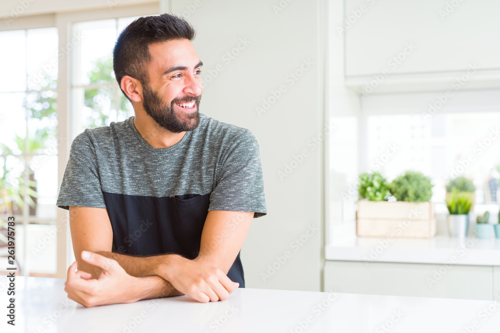 Handsome hispanic man wearing casual t-shirt at home looking away to side with smile on face, natural expression. Laughing confident. Handsome hispanic man wearing casual t-shirt at home looking away to side with smile on face, natural expression. Laughing confident.