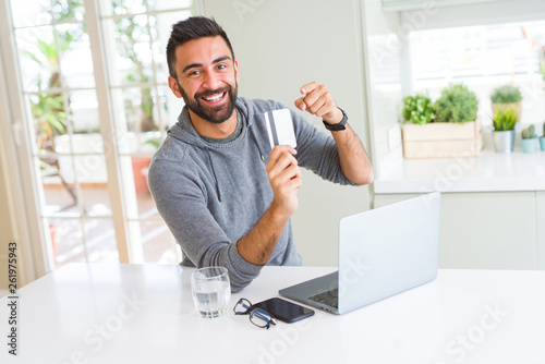 Handsome man smiling using credit card as payment metod when shopping online using laptop photo