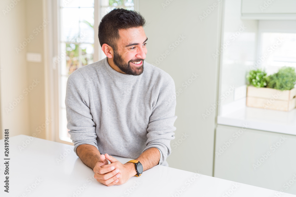 Handsome hispanic man wearing casual sweater at home looking away to side with smile on face, natural expression. Laughing confident.