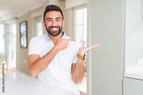 Handsome hispanic man casual white t-shirt at home amazed and smiling to the camera while presenting with hand and pointing with finger. © Krakenimages.com