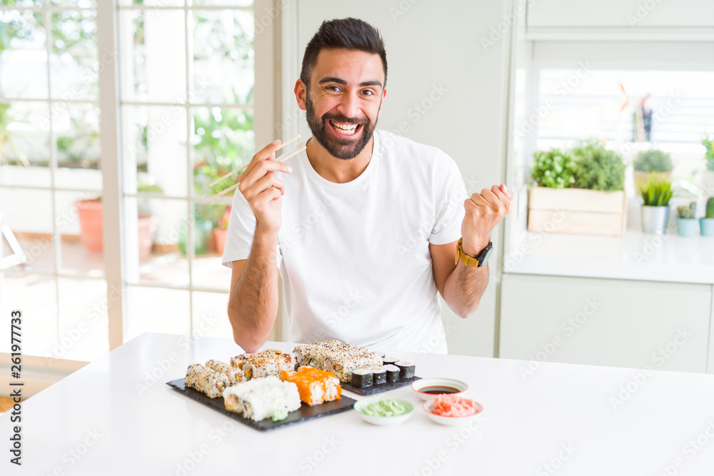Handsome hispanic man eating asian sushi using chopsticks screaming proud and celebrating victory and success very excited, cheering emotion