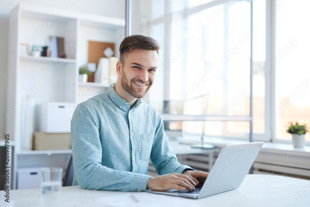 Portrait of handsome young man working in office and smiling happily at camera, copy space Portrait of handsome young man working in office and smiling happily at camera, copy space