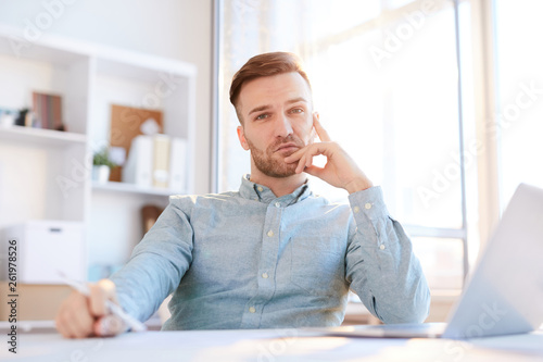 Photography Portrait of handsome man looking at camera while sitting at workplace lit by sun
