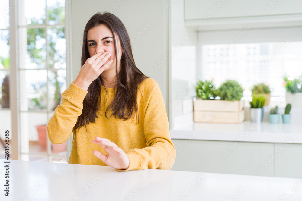Beautiful young woman wearing yellow sweater smelling something stinky and disgusting, intolerable smell, holding breath with fingers on nose. Bad smells concept. Beautiful young woman wearing yellow sweater smelling something stinky and disgusting, intolerable smell, holding breath with fingers on nose. Bad smells concept.