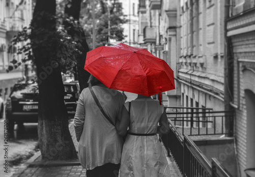 people walk under an umbrella in the rain down the old street in black and white style photo