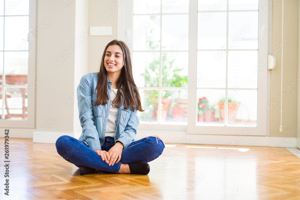 Beautiful young woman sitting on the floor at home looking away to side with smile on face, natural expression. Laughing confident. Beautiful young woman sitting on the floor at home looking away to side with smile on face, natural expression. Laughing confident.