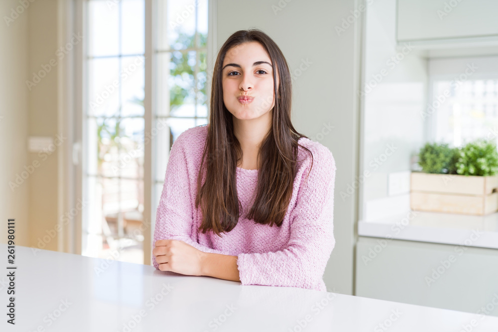 Beautiful young woman wearing pink sweater puffing cheeks with funny face. Mouth inflated with air, crazy expression. Beautiful young woman wearing pink sweater puffing cheeks with funny face. Mouth inflated with air, crazy expression.
