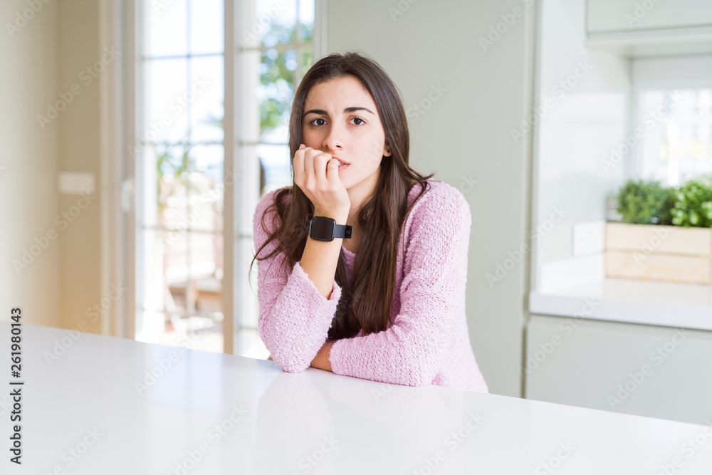 Beautiful young woman wearing pink sweater looking stressed and nervous with hands on mouth biting nails. Anxiety problem. Beautiful young woman wearing pink sweater looking stressed and nervous with hands on mouth biting nails. Anxiety problem.