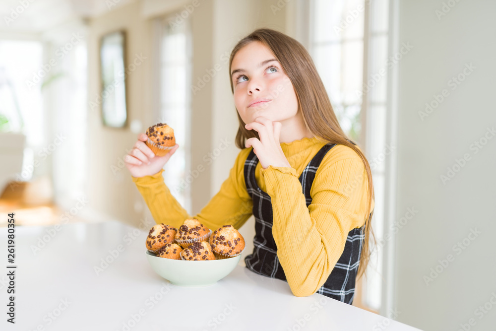 Beautiful young girl eating chocolate chips muffins serious face thinking about question, very confused idea Beautiful young girl eating chocolate chips muffins serious face thinking about question, very confused idea