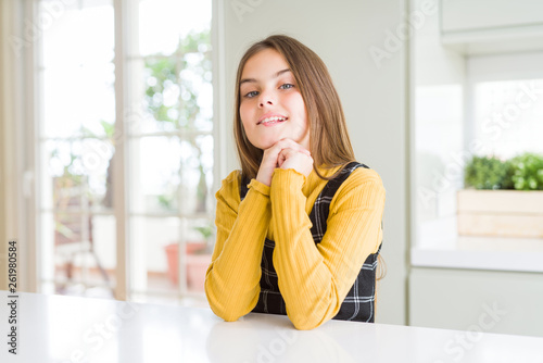 Young beautiful blonde kid girl wearing casual yellow sweater at home laughing nervous and excited with hands on chin looking to the side