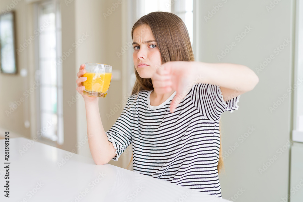 Beautiful young girl kid drinking a glass of fresh orange juice with angry face, negative sign showing dislike with thumbs down, rejection concept Beautiful young girl kid drinking a glass of fresh orange juice with angry face, negative sign showing dislike with thumbs down, rejection concept