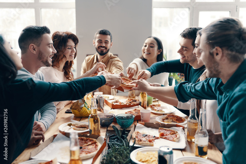 Hurry up to pick the best slice! Group of young people in casual wear picking pizza and smiling while having a dinner party indoors © gstockstudio