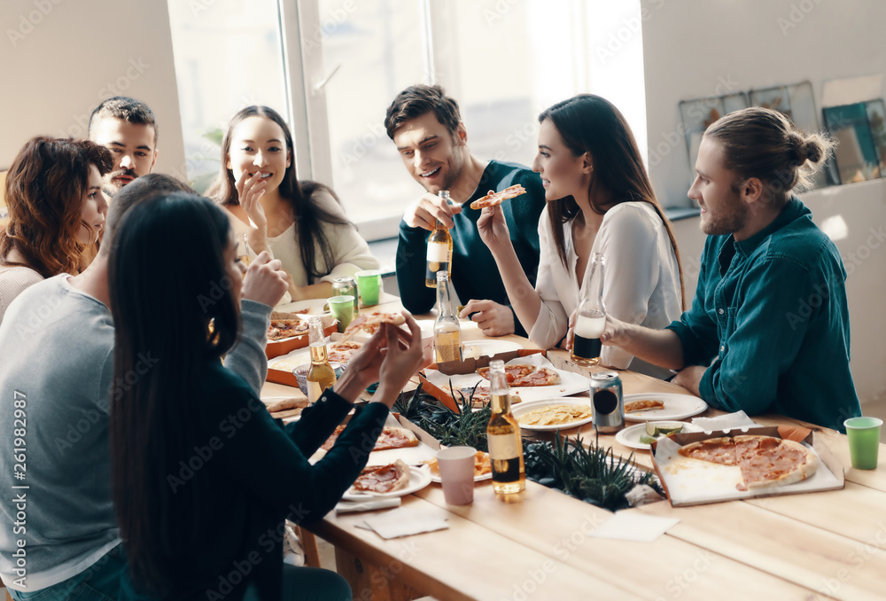 Great evening with friends. Group of young people in casual wear eating pizza and smiling while having a dinner party indoors Great evening with friends. Group of young people in casual wear eating pizza and smiling while having a dinner party indoors