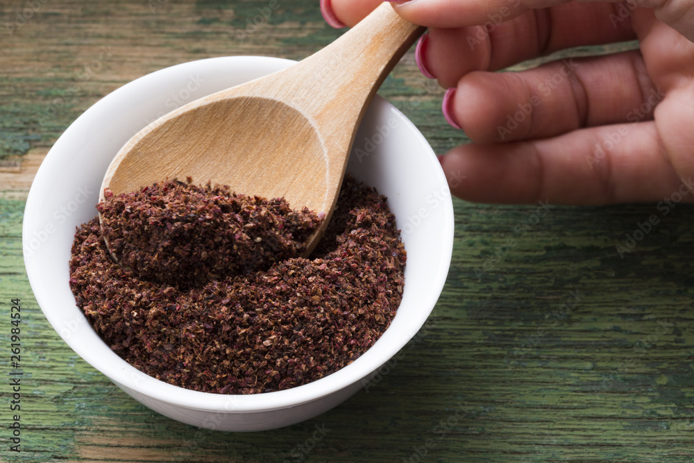 Woman taking sumac spice with wooden spoon from white bowl Woman taking sumac spice with wooden spoon from white bowl