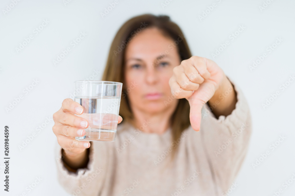 Middle age woman drinking glass of water isolated background with angry face, negative sign showing dislike with thumbs down, rejection concept Middle age woman drinking glass of water isolated background with angry face, negative sign showing dislike with thumbs down, rejection concept
