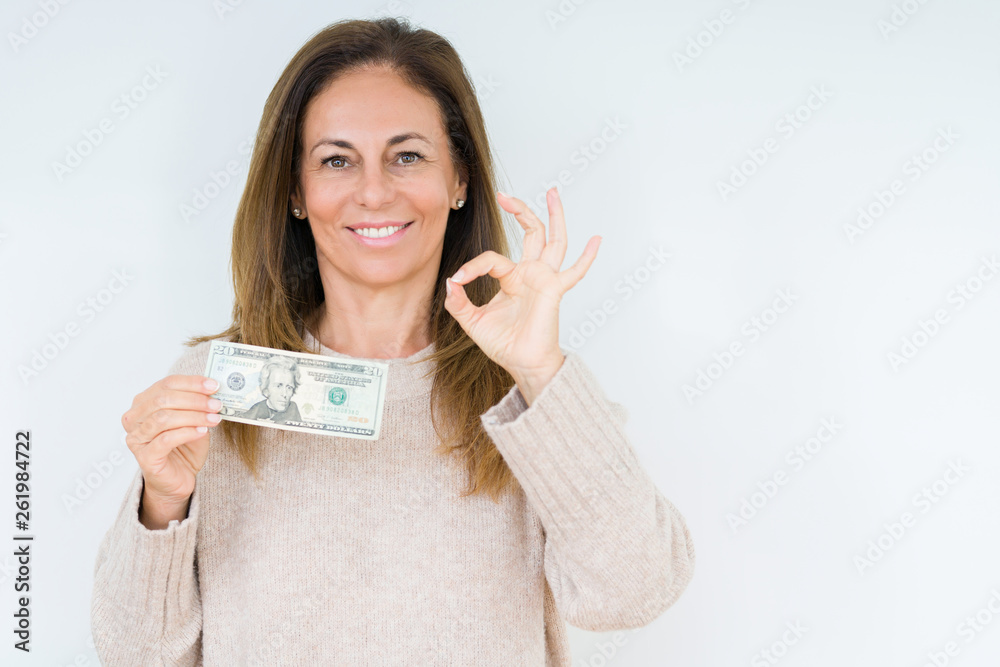 Middle age woman holding 20 dollars bank note over isolated background doing ok sign with fingers, excellent symbol Middle age woman holding 20 dollars bank note over isolated background doing ok sign with fingers, excellent symbol