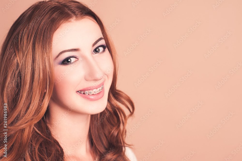 Fototapeta premium Smiling girl 16-17 year old wearing braces over beige background close up. Healthy dental smile. Looking at camera.