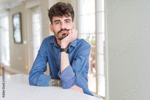 Young man wearing casual shirt sitting on white table thinking looking tired and bored with depression problems with crossed arms.