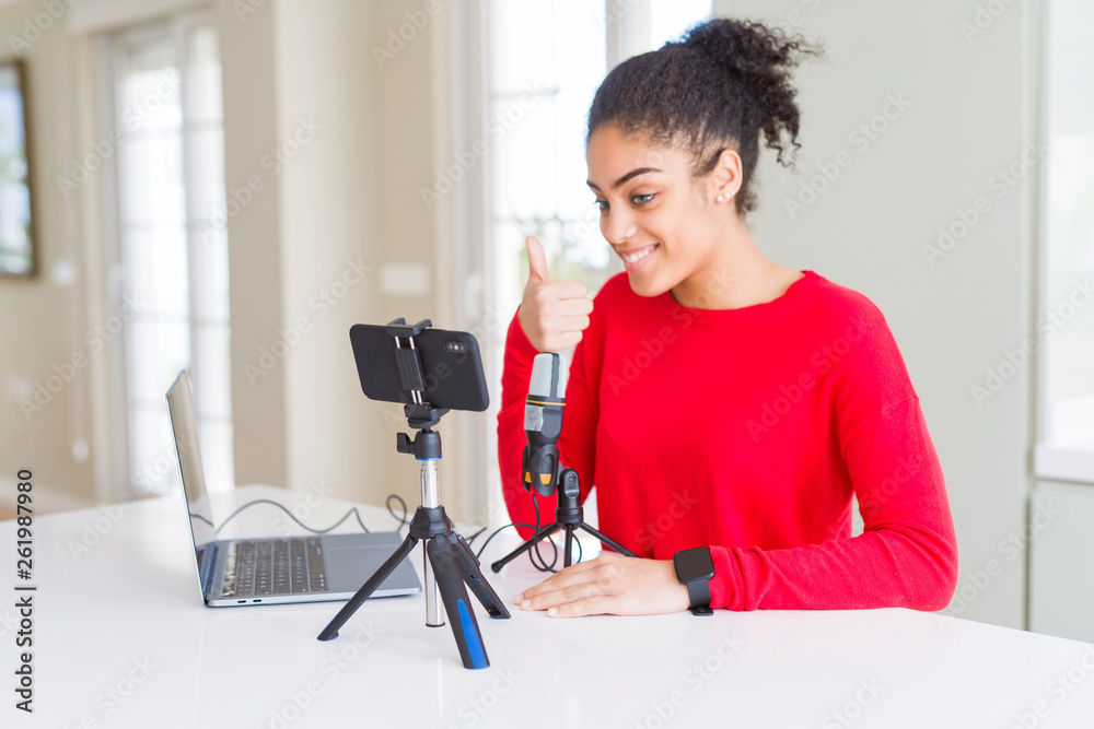 Young african american woman doing video call using smartphone camera and microphone doing happy thumbs up gesture with hand. Approving expression looking at the camera with showing success. Young african american woman doing video call using smartphone camera and microphone doing happy thumbs up gesture with hand. Approving expression looking at the camera with showing success.