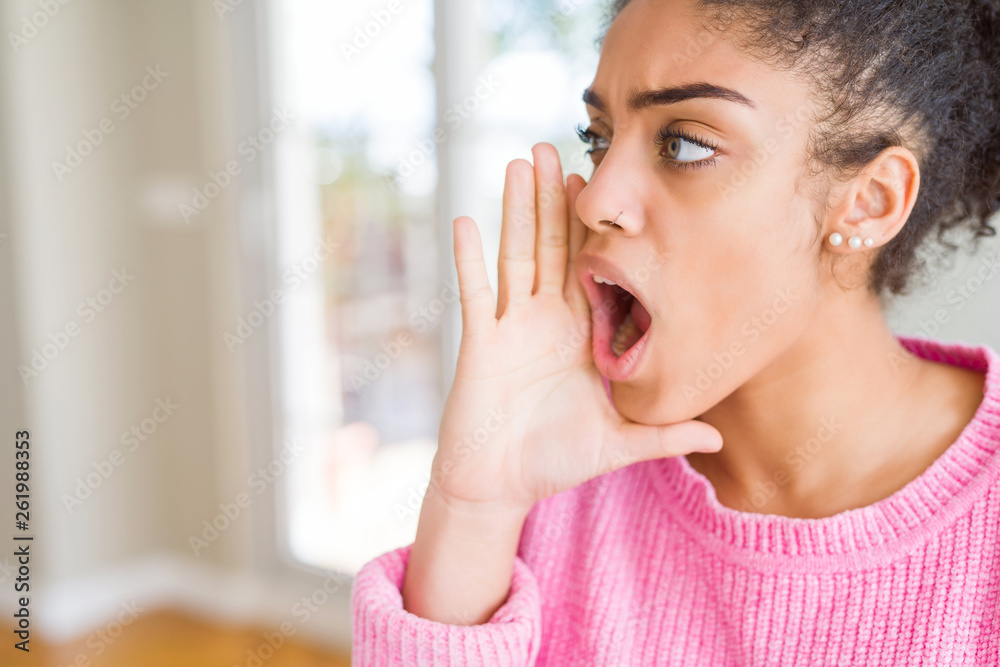 Beautiful young african american woman with afro hair shouting and screaming loud to side with hand on mouth. Communication concept. Beautiful young african american woman with afro hair shouting and screaming loud to side with hand on mouth. Communication concept.