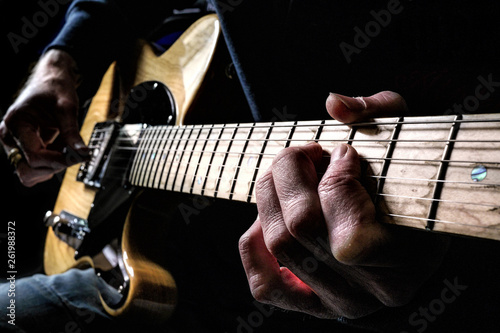 Guitarist playing a natural wood electric guitar in moody light with focus on fingers of fret hand on maple fingerboard. photo