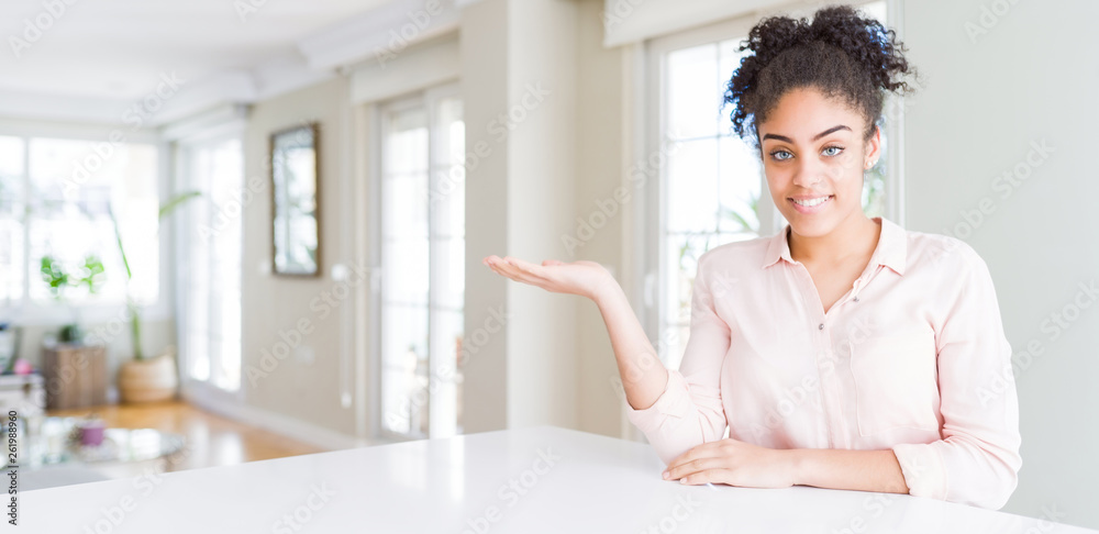 Wide angle of beautiful african american woman with afro hair smiling cheerful presenting and pointing with palm of hand looking at the camera. Wide angle of beautiful african american woman with afro hair smiling cheerful presenting and pointing with palm of hand looking at the camera.