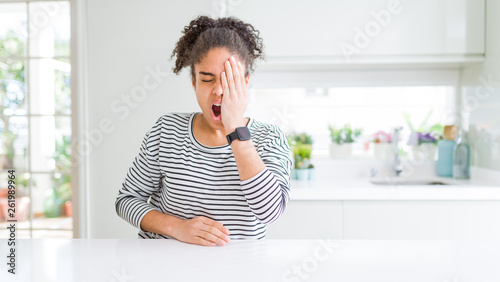 Beautiful african american woman with afro hair wearing casual striped sweater Yawning tired covering half face  eye and mouth with hand. Face hurts in pain.